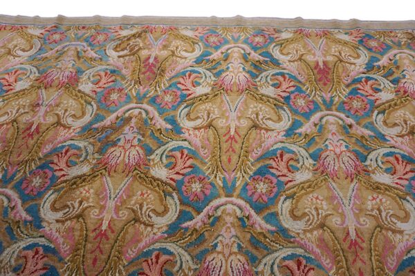 Close-up of a medium-pile rug featuring symmetrical scrollwork in tan, pink, blue, and cream colors.