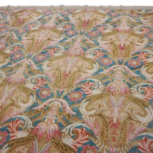 High-pile rug featuring scrolling floral and baroque designs in tan, teal, pink, and cream colors.