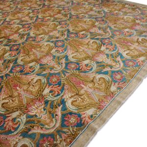 A detailed, high-pile rug featuring scrolling floral patterns in gold, teal, pink, and tan colors on a white background.