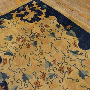 Gold rug with a navy blue border, detailed with rust flowers and teal leaves on wide plank flooring.