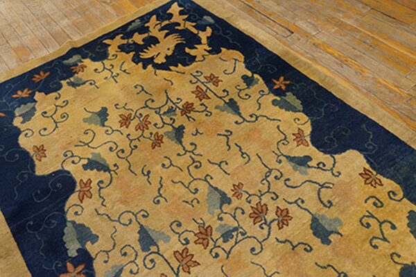 Gold rug with a navy blue border, detailed with rust flowers and teal leaves on wide plank flooring.