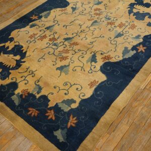 Gold and navy rug with floral vines and stylized border motifs resting on worn wooden planks.