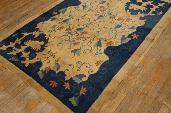 Gold and navy rug with floral vines and stylized border motifs resting on worn wooden planks.