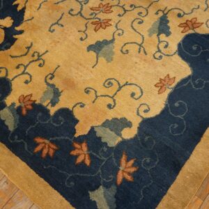 Navy and gold rug featuring a dragon and floral pattern, framed by a tan border on distressed wood floors.