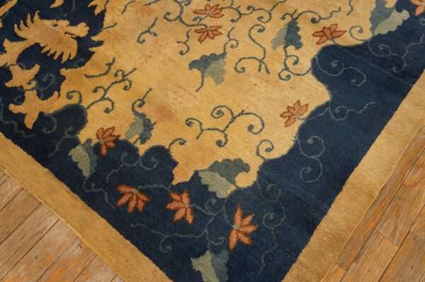 Navy and gold rug featuring a dragon and floral pattern, framed by a tan border on distressed wood floors.