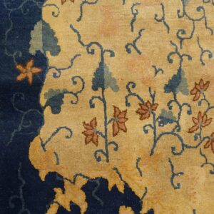 Plush gold and navy rug detail showing scrolling blue vines and pinkish-brown floral motifs on wood floor.