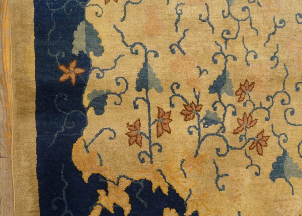 Plush gold and navy rug detail showing scrolling blue vines and pinkish-brown floral motifs on wood floor.
