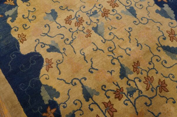 Tan pile rug with a navy border and dense floral pattern in blue, pink, and reddish-brown colors.