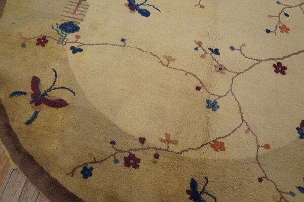 Beige rug detail showing maroon butterflies, blue flowers, and a dark brown border on wood planks.