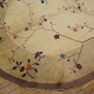 Round beige rug with a dark brown outer border and sparse burgundy and blue floral pattern on wood.