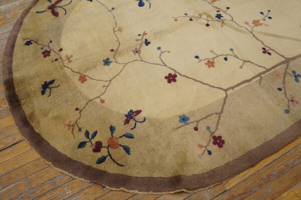 Round beige rug with a dark brown outer border and sparse burgundy and blue floral pattern on wood.