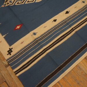Blue flatweave rug with beige geometric borders and dark stripes laid on worn wood flooring.