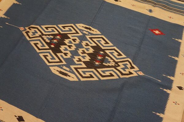 Flat-weave rug with a blue field and a cream border framing geometric greek key and diamond designs.