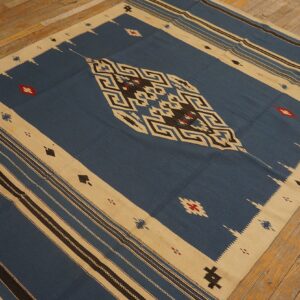 Blue, tan, and black flat-weave rug featuring geometric patterns and red accents on wood flooring.