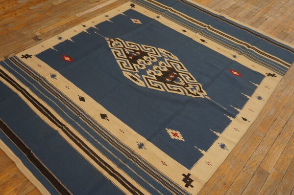 Blue, tan, and black flat-weave rug featuring geometric patterns and red accents on wood flooring.