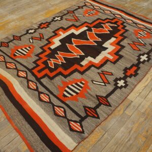 Geometric flatweave rug in gray, bright orange, brown, and white on distressed wooden flooring.