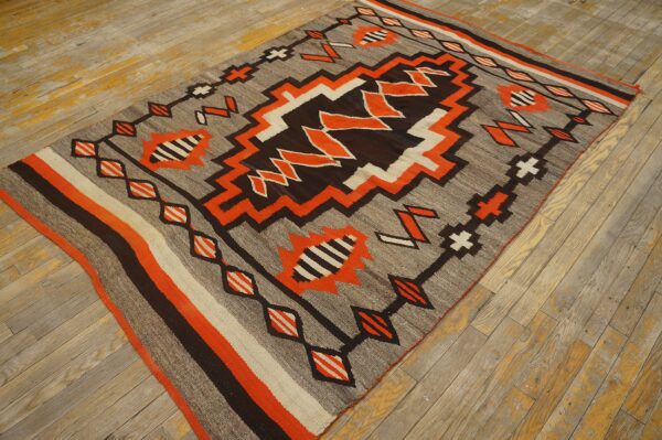 Geometric flatweave rug in gray, bright orange, brown, and white on distressed wooden flooring.