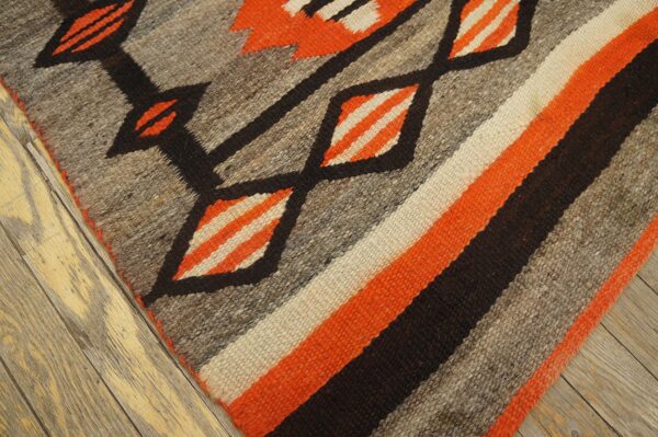 Geometric rug with orange, gray, black, and cream diagonal stripes rests on worn, light wood flooring.