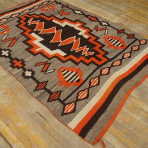 Geometric flatweave rug in gray, dark brown, orange, and white displayed on distressed wood planks.