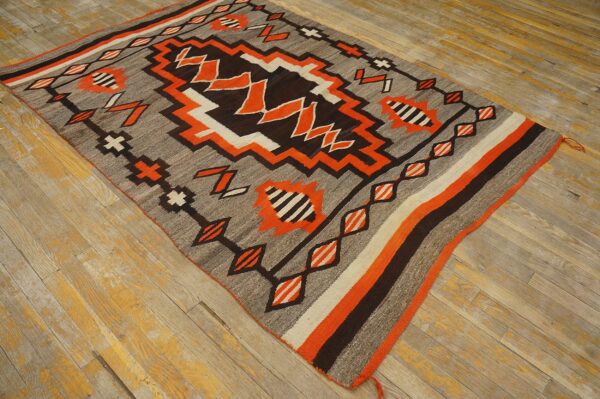 Geometric flatweave rug in gray, dark brown, orange, and white displayed on distressed wood planks.
