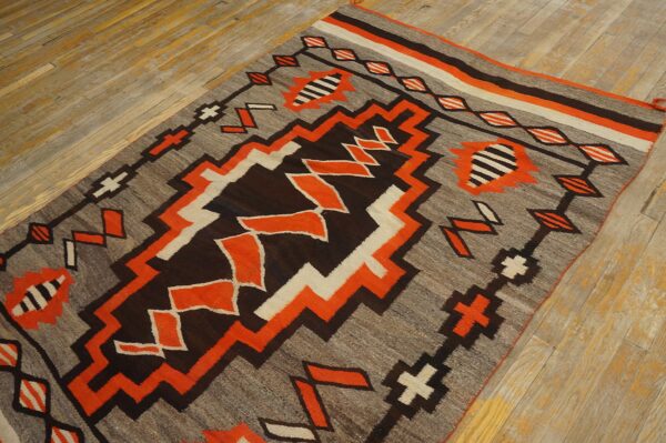 Geometric rug in gray, orange, brown, and cream with a zigzag motif rests on wooden planks.