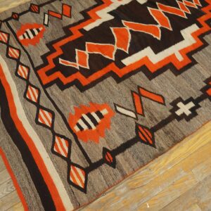 Flatweave rug with zigzag patterns in gray, brown, orange, and off-white rests on worn wood planks.
