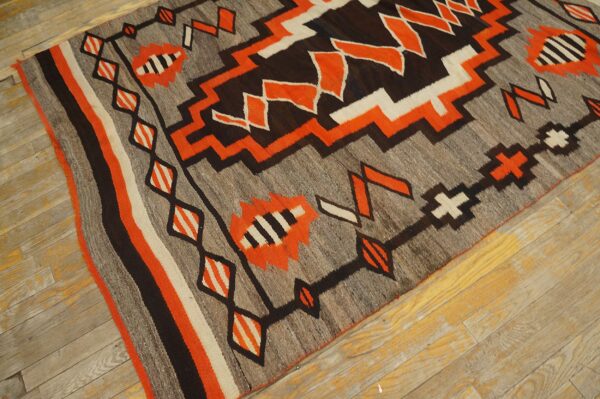Flatweave rug with zigzag patterns in gray, brown, orange, and off-white rests on worn wood planks.