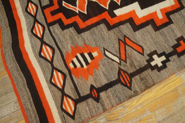 Flatwoven rug with bold orange, black, and cream geometric patterns rests on a wood floor.