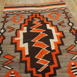 Low pile rug with bold orange, brown, grey, and white geometric designs on distressed wood floorboards.