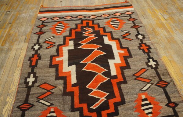 Low pile rug with bold orange, brown, grey, and white geometric designs on distressed wood floorboards.