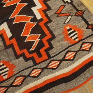 Gray, orange, black, and cream flatweave rug with stepped geometric patterns resting on wood planks.