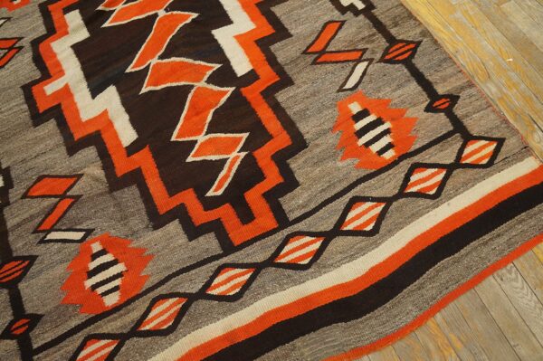 Gray, orange, black, and cream flatweave rug with stepped geometric patterns resting on wood planks.