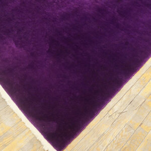 A corner of a velvety purple rug with cream fringe rests on light, worn wooden floors.