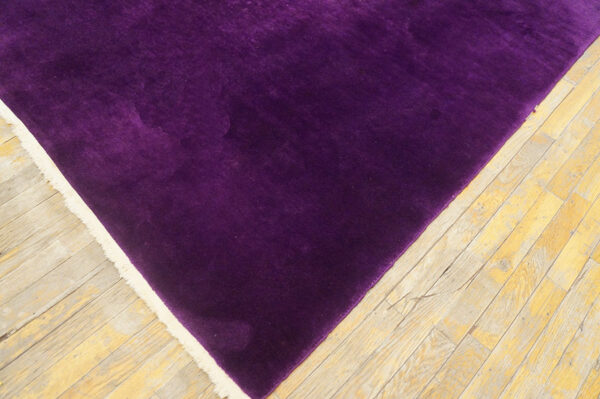 A corner of a velvety purple rug with cream fringe rests on light, worn wooden floors.