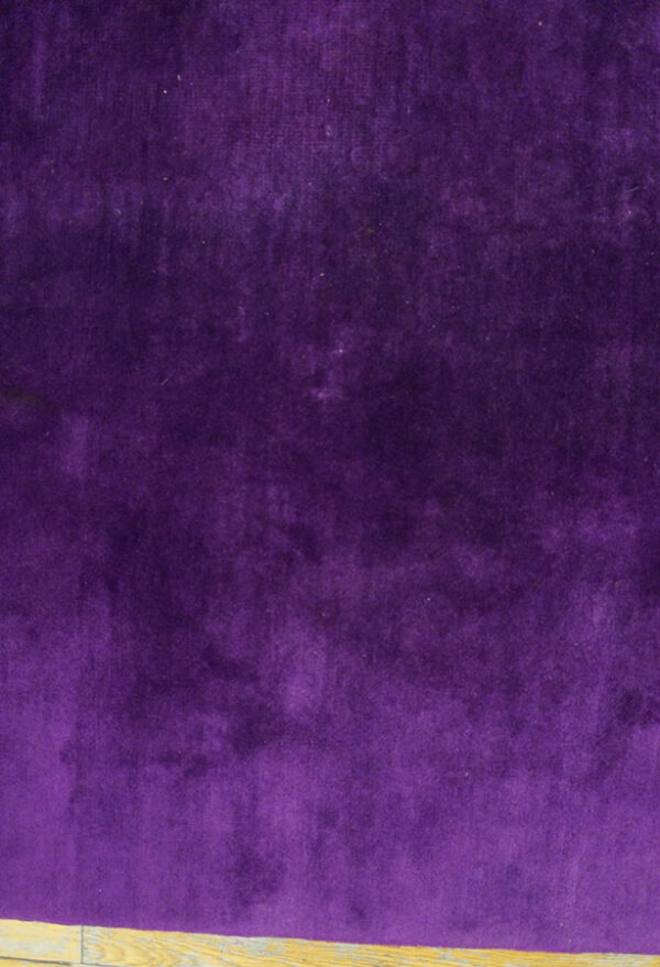 Plush, deep purple solid-colored rug texture shown in close-up above light wood flooring.