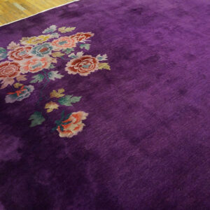 A velvety purple rug with a corner bouquet of pink, peach, and blue flowers rests on hardwood flooring.