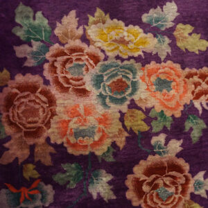 Velvety purple rug displaying colorful clustered flowers in peach, teal, yellow, and crimson hues.