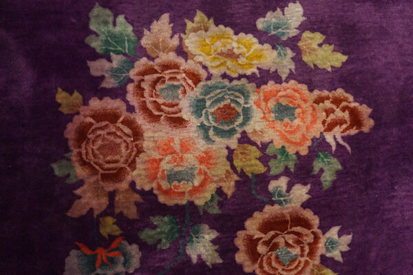Velvety purple rug displaying colorful clustered flowers in peach, teal, yellow, and crimson hues.