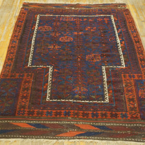 Geometric rug with a stepped central niche design in red and blue tones resting on wood plank flooring.