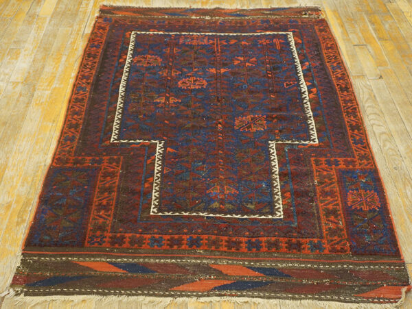 Geometric rug with a stepped central niche design in red and blue tones resting on wood plank flooring.