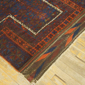 Close-up of a tribal geometric rug featuring red, blue, and maroon colors on worn wooden floorboards.