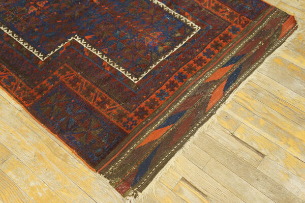 Close-up of a tribal geometric rug featuring red, blue, and maroon colors on worn wooden floorboards.