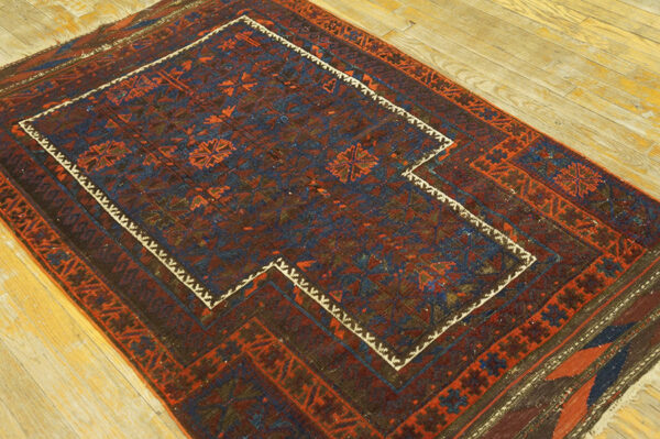 Red and blue geometric rug with a stepped central panel bordered by a bright white zigzag design on wood floors.