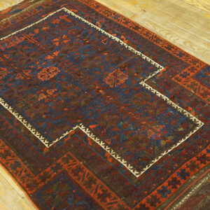 Low-pile geometric rug in earthy reds and blues featuring a stepped medallion on a wood floor.