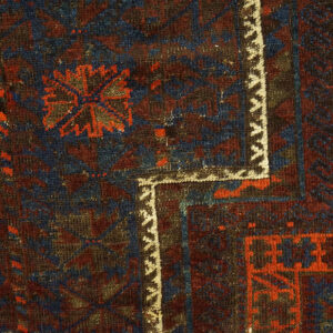 Dark, low-pile rug corner featuring geometric patterns in navy, deep red, and a contrasting cream border.