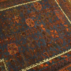 Worn, low-pile rug displaying intricate geometric patterns in navy, rust, and brown tones.