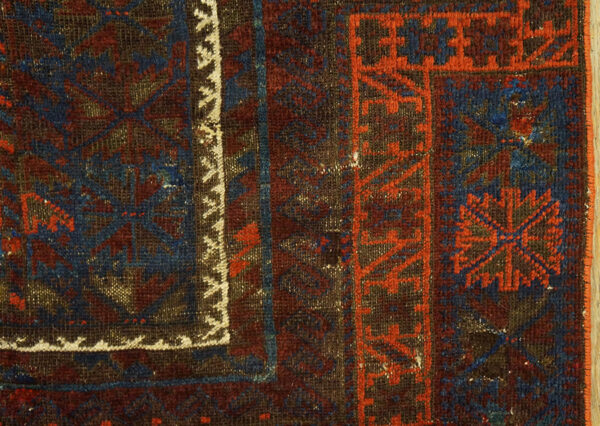 Close-up of a tightly woven, geometric rug pattern in dark blue, maroon, orange, and brown tones.