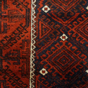 Deep red and navy rug detail showing a plush pile and intricate geometric diamond patterns.
