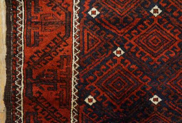 Deep red and navy rug detail showing a plush pile and intricate geometric diamond patterns.