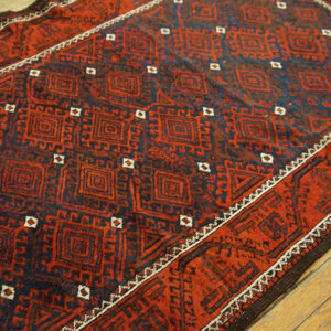 Red and navy geometric rug featuring repeating squares rests on light brown hardwood flooring.